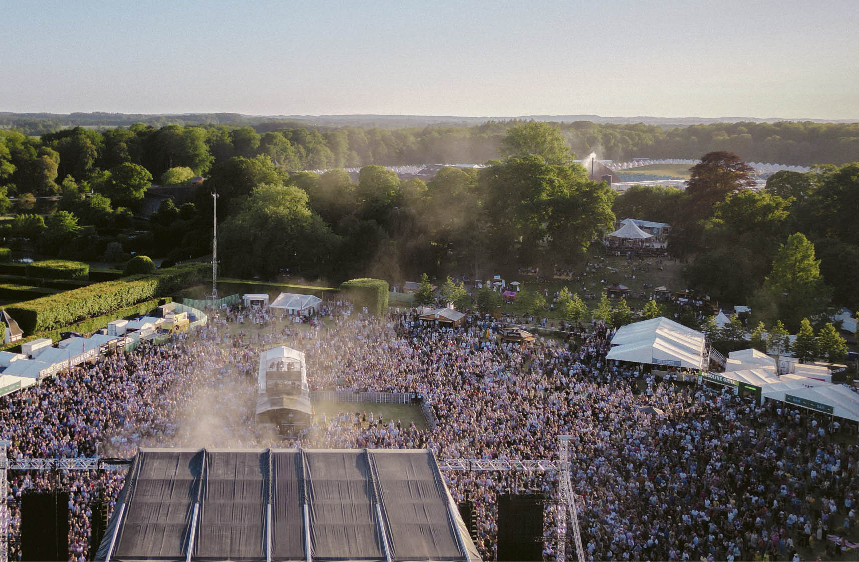 A large crowd of people are gathered in a field, watching a concert. Description generated by AI